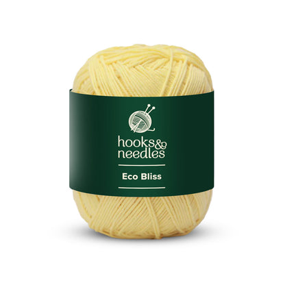 A ball of organic cotton yarn labeled "Eco Bliss Yarn 50g" features a dark green band, showcasing its eco-friendly charm.