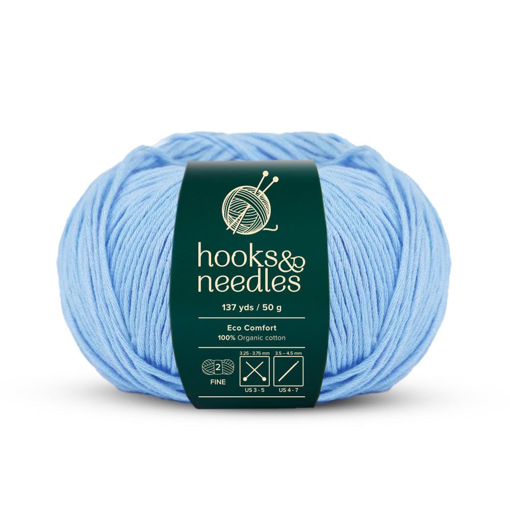 A skein of light blue yarn featuring a green label that reads "hooks & needles: Eco Comfort Yarn 50g, 100% Organic Cotton, 137 yds." Ideal for sustainable knitting, this environmentally friendly yarn delivers both quality and ethical consciousness for your creative endeavors.