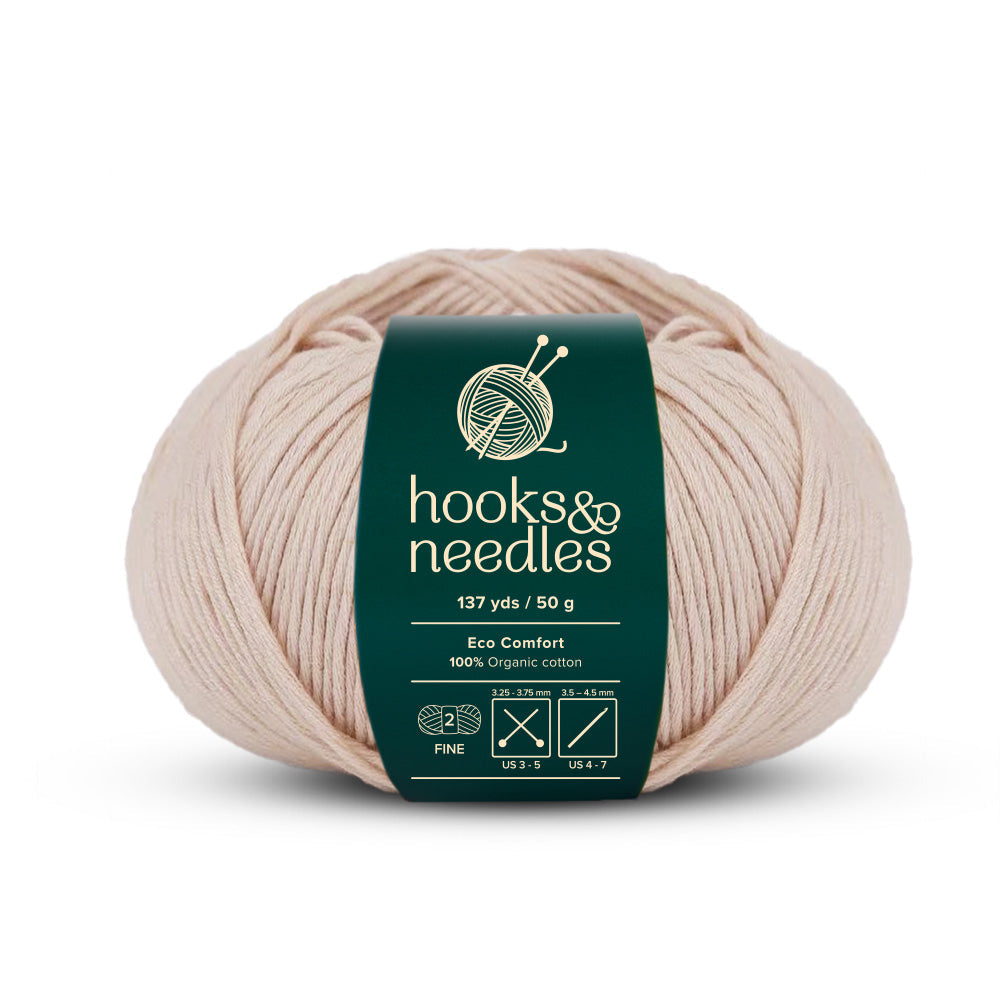 A cream-colored ball of yarn with a dark green "hooks & needles" label, highlighting 137 yards and 50 grams, made entirely from eco-friendly organic cotton, named Eco Comfort Yarn 50g.