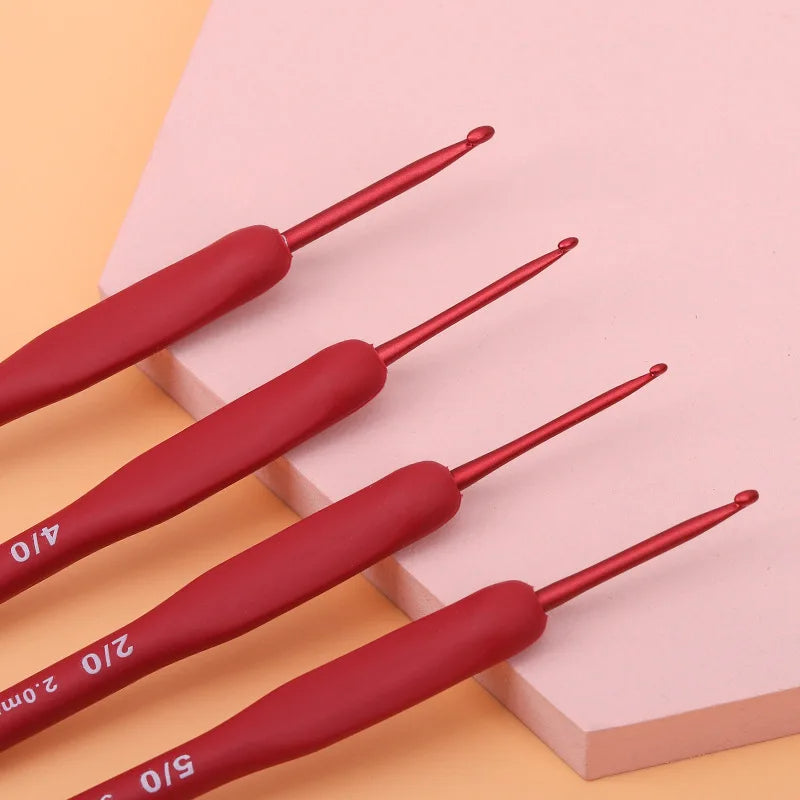 A set of four red ergonomic crochet hooks from the 'Ergonomic Crochet Hook Set 9 Pcs with Soft Grip Handles' collection are arranged diagonally on a light pink surface, providing a comfortable crocheting experience.