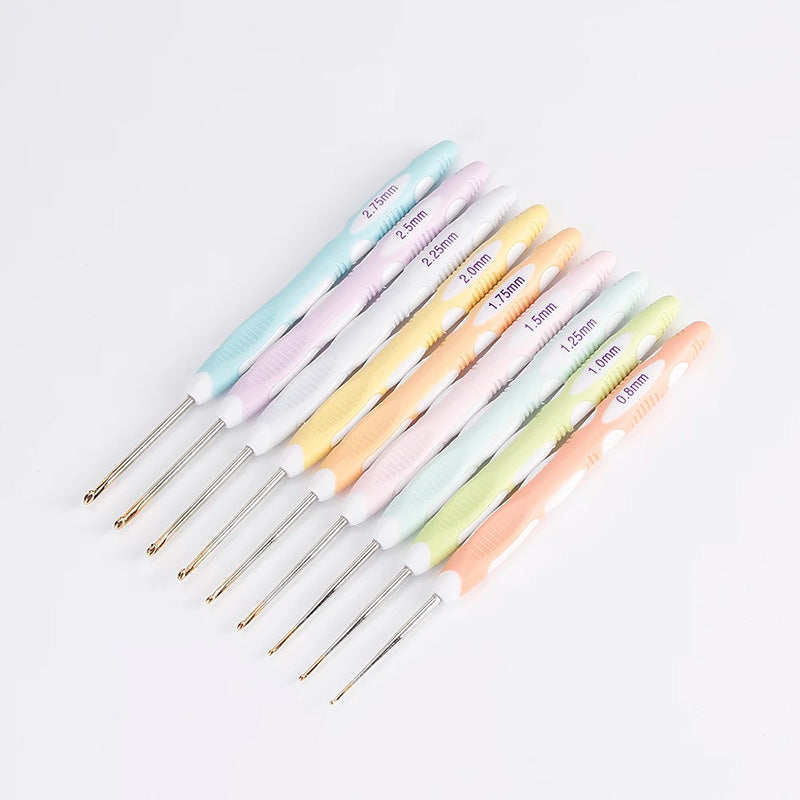 The Crochet Hook Set 9 Pcs with Soft Grip Handles features nine vibrant hooks laid out in a row, each designed with an ergonomic grip. These hooks are color-coded and labeled with sizes ranging from 0.6mm to 2.5mm for your crafting ease.