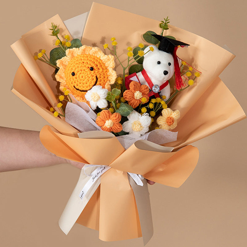 A hand presents the Doctor Bear Graduation Season Crochet Bouquet, showcasing a lively sun and Doctor Bear among charming animal figures. The bouquet is adorned with yellow and orange flowers and tastefully wrapped in peach paper, making it an ideal addition to any graduation celebration.