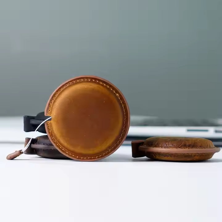 Close-up of a handmade leather mini tape measure on a white surface in front of a blurred background.