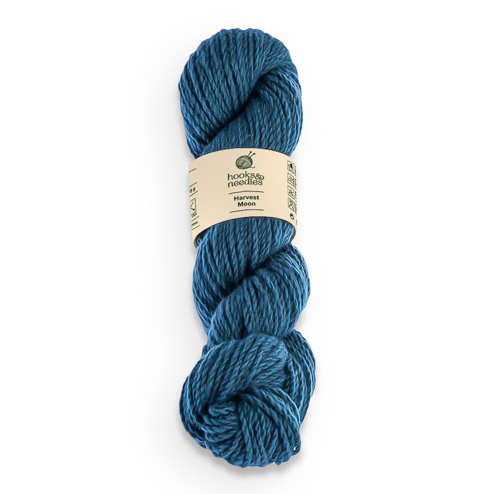A skein of 100% Wool yarn, in blue, with a label reading "Harvest Moon" from the brand "hooks & strings".