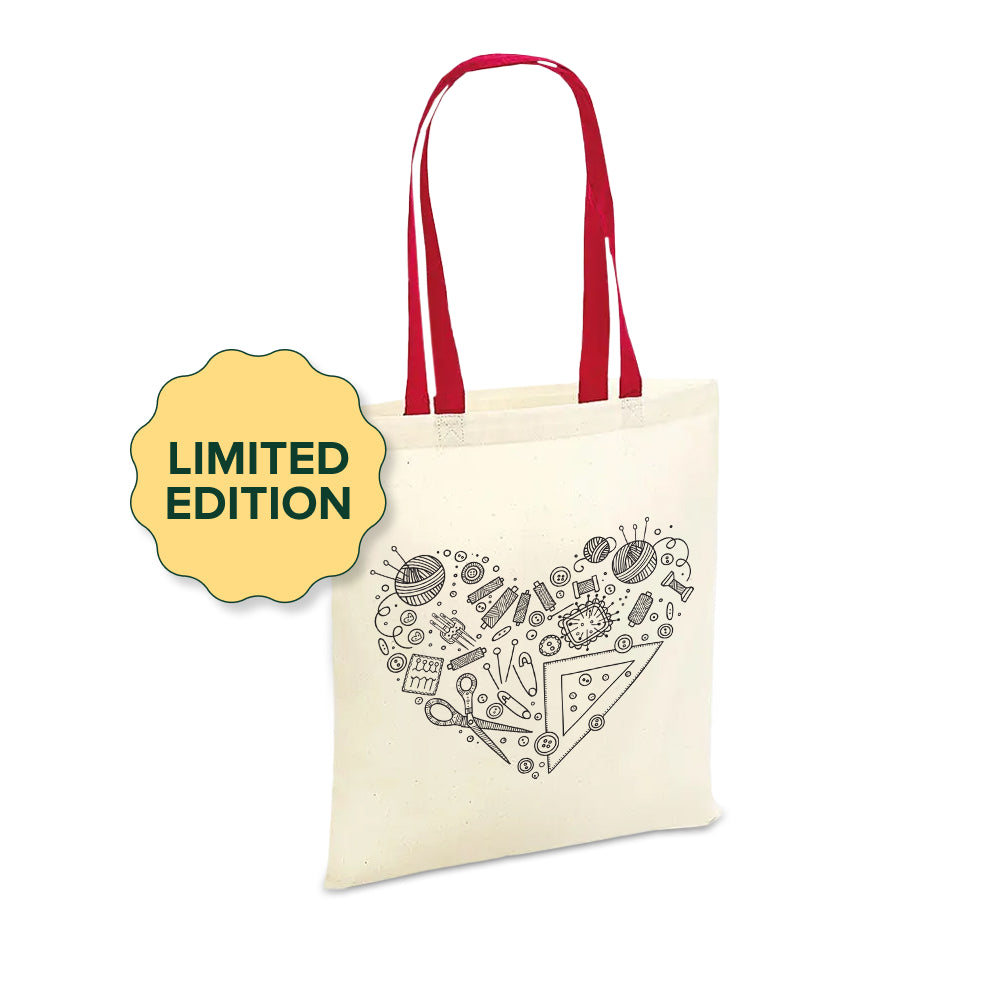 A cream-colored Limited Edition Mother's Day tote bag with red handles, featuring a black sketch of various crafting supplies arranged in a heart shape, marked with a "limited edition" label.