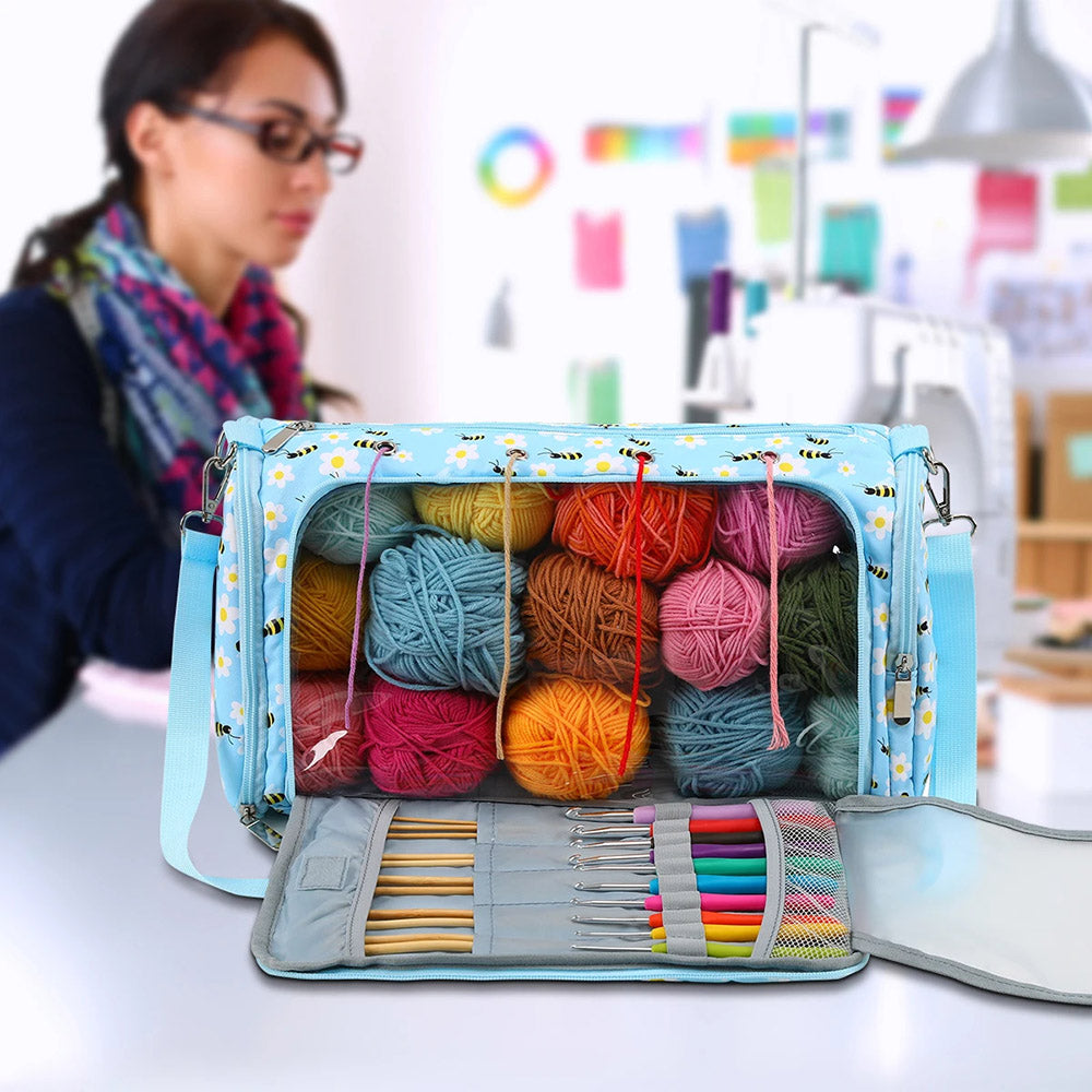 A Yarn Bag - Storage Organizer brimming with crocheting accessories, featuring vibrant yarn balls and crochet hooks, sits prominently in the foreground while a person works on a computer in a brightly lit room.