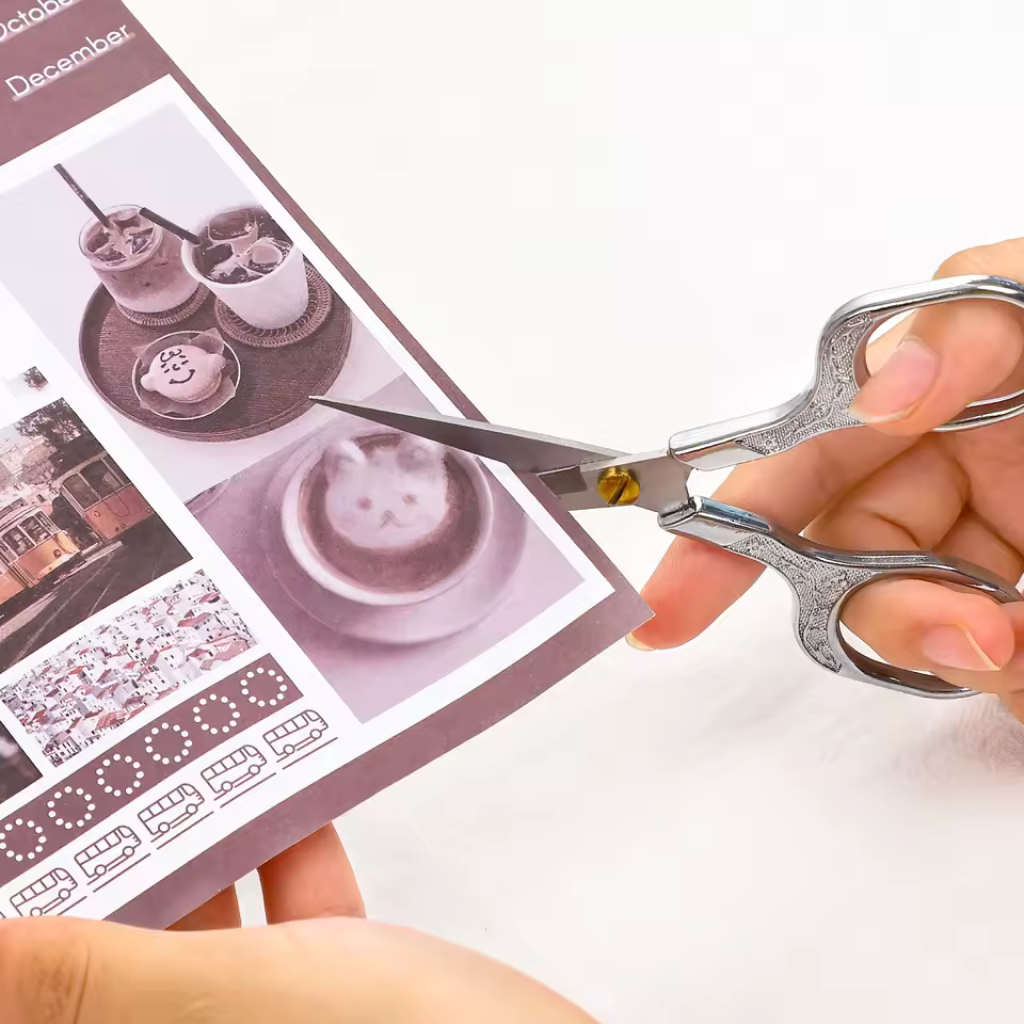 A person uses Retro Stainless Steel Yarn Scissors to cut a sheet of paper with photos of latte art and other images.