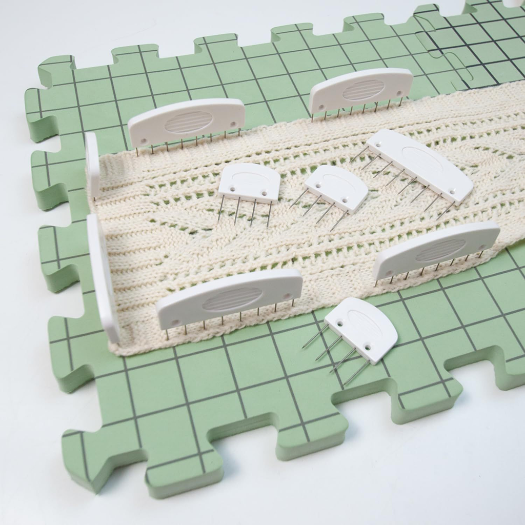 A knitted piece is pinned to Knitting Crocheting Blocking Mats with grid lines, secured in place using several white blocking pins.