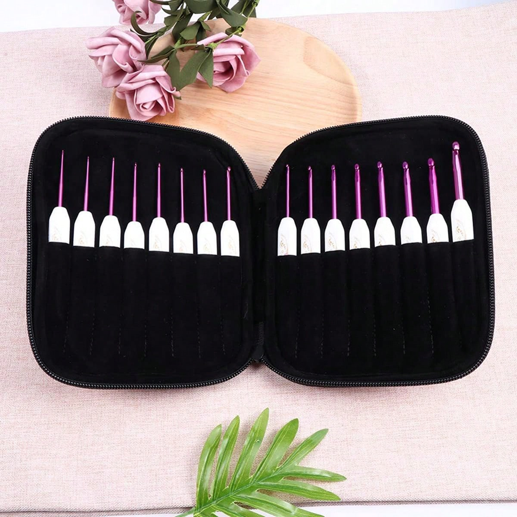 A black zippered case holding the Crochet Hook Set 16 Pcs with Case in purple and white is open on a table, surrounded by artificial flowers and a green leaf.
