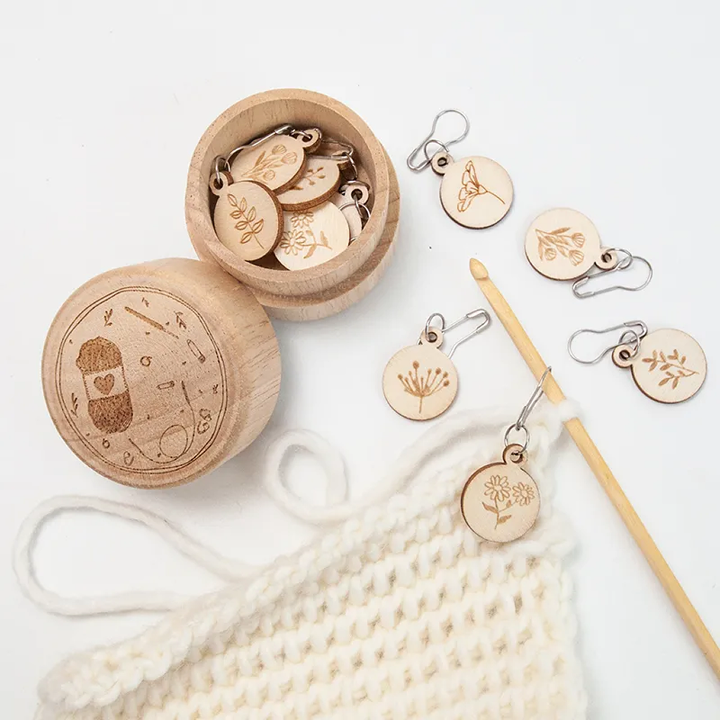 The Wooden Flower Stitch Markers with Storage Box 8Pcs includes a round box with an engraved lid, containing wooden markers in leaf and flower shapes. Durable storage keeps your markers organized and protected for all your knitting projects.