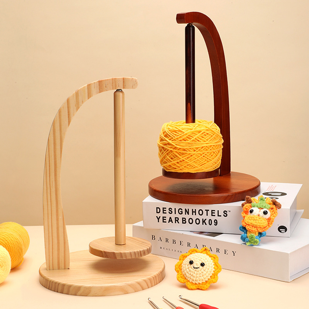The Levitating Premium Yarn Holder, shown in natural and dark wood with a yellow yarn ball, crocheted toys, books, and hooks on a beige background, keeps your yarn tangle-free—ideal for organized crafters.