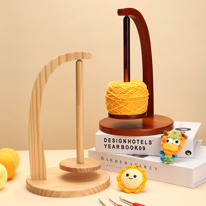 The Levitating Premium Yarn Holder, shown in natural and dark wood with a yellow yarn ball, crocheted toys, books, and hooks on a beige background, keeps your yarn tangle-free—ideal for organized crafters.