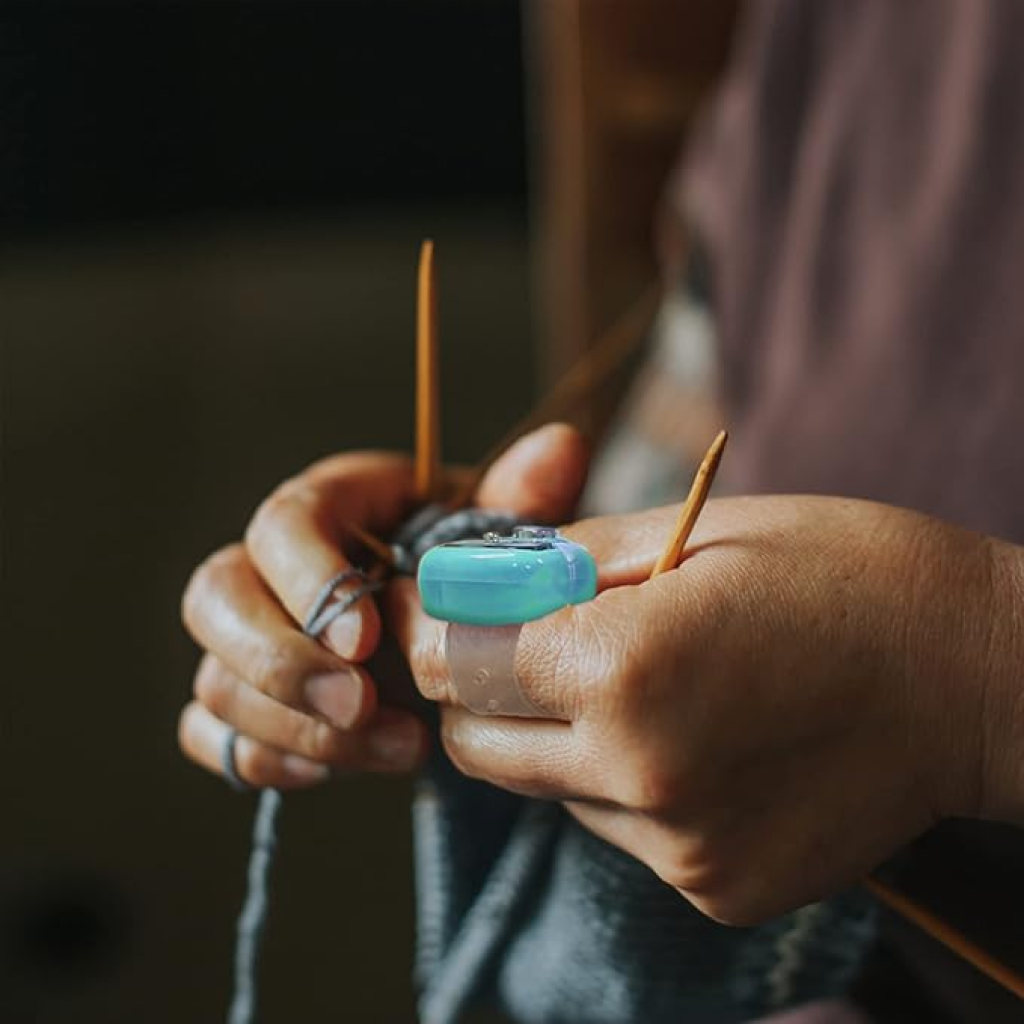 A person knitting with wooden needles while wearing the Digital Row Counter on their finger for easy and convenient tracking.