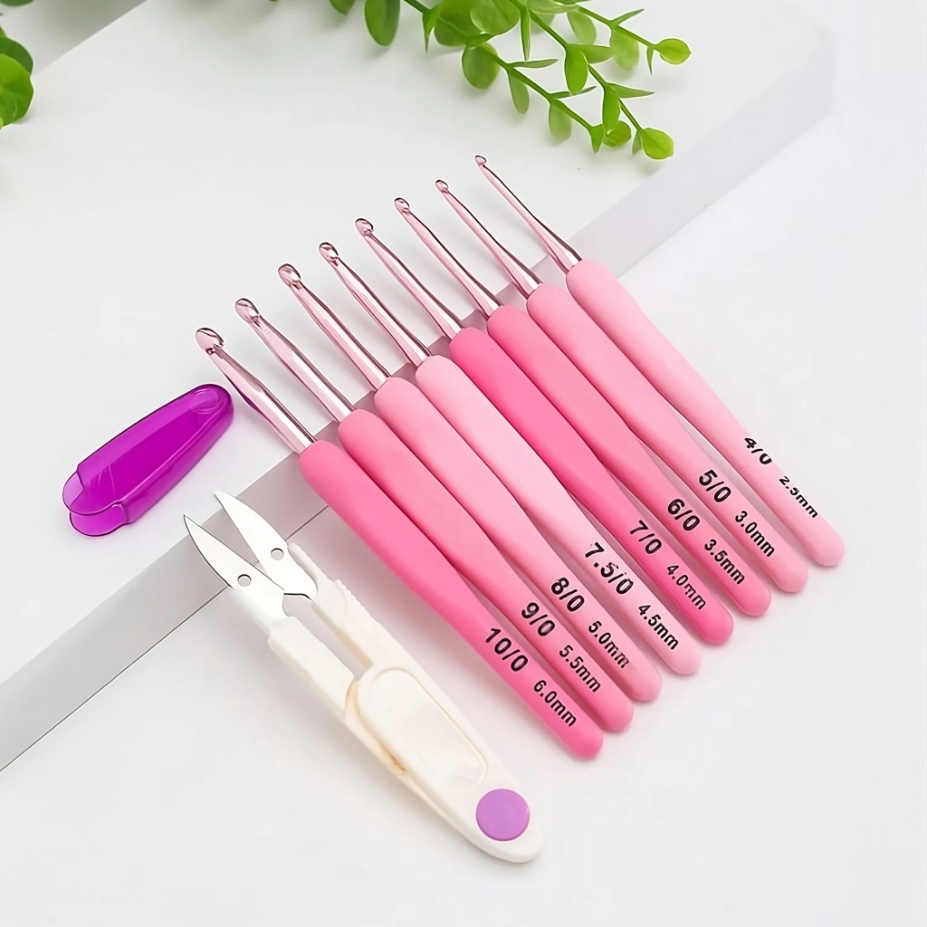 The Ergonomic Crochet Hook Set 9 Pcs with Case includes nine pink-handled, size-labeled ergonomic hooks, thread snips, and a purple needle case displayed on a white surface with green leaves—ideal for pain-free crocheting.