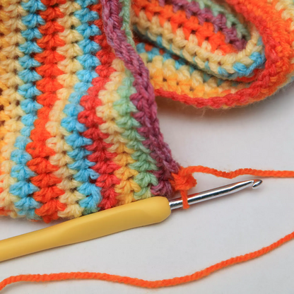 An Ergonomic Crochet Hook Set 9 Pcs, with a durable aluminum hook and yellow handle, rests on a vibrant striped crochet project featuring orange, yellow, pink, blue, and green yarn.
