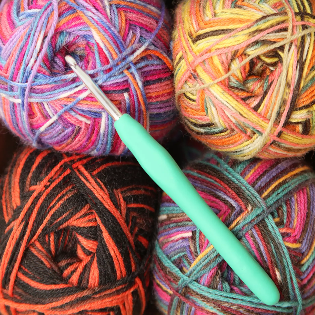 Four multicolored yarn balls are grouped together with the Ergonomic Crochet Hook Set 9 Pcs, featuring a durable aluminum hook and a soft grip handle, resting on top.