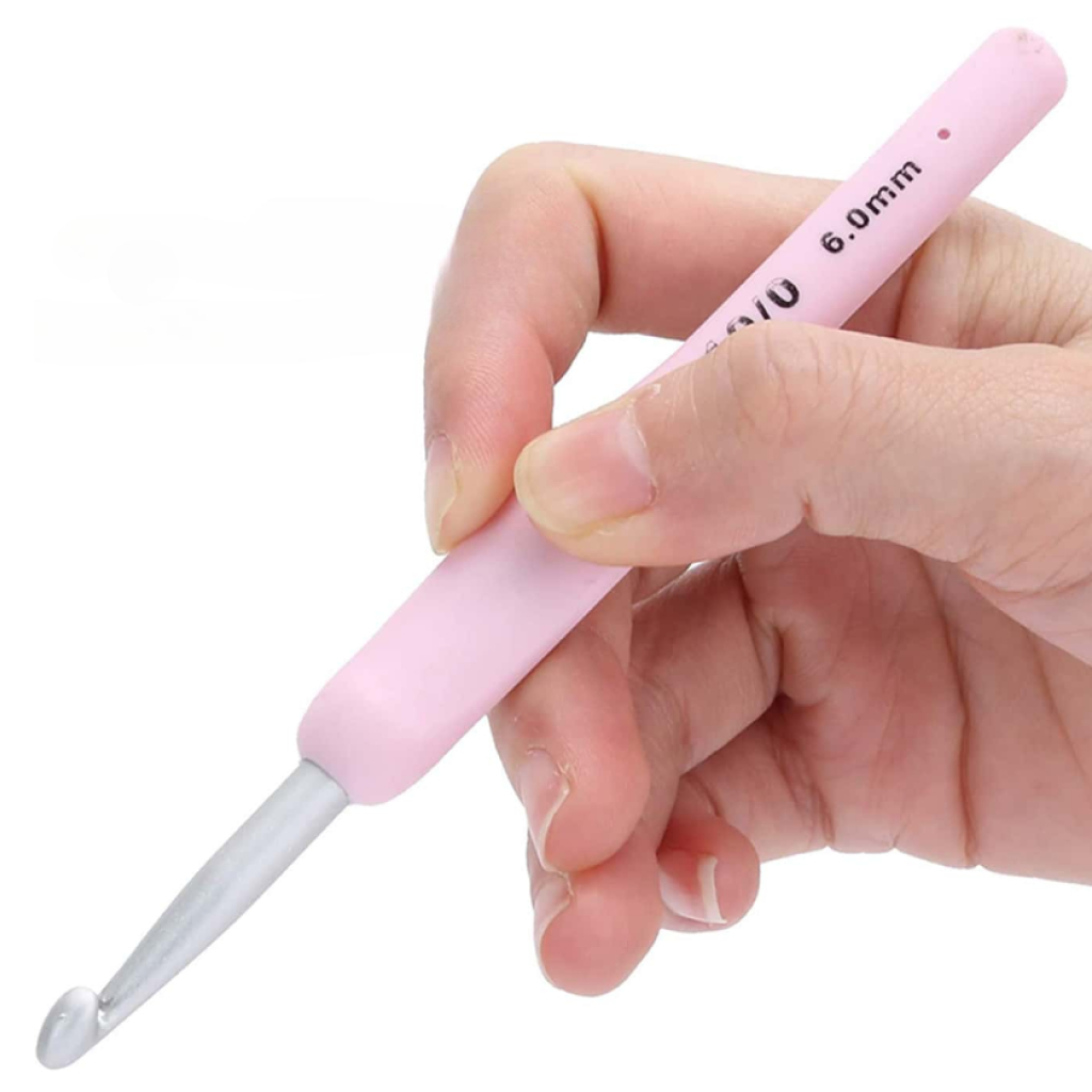 A hand holding a 6.0 mm ergonomic crochet hook with a pink handle from the Ergonomic Crochet Hook Set 9 Pcs with Case, metal tip facing forward—ideal for comfortable, pain-free crocheting.