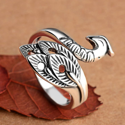 The Yarn Tension Control Ring, crafted from stainless steel and designed with leaf-shaped patterns that mimic a curled snake, is showcased on a brown surface with a dried leaf beneath it.