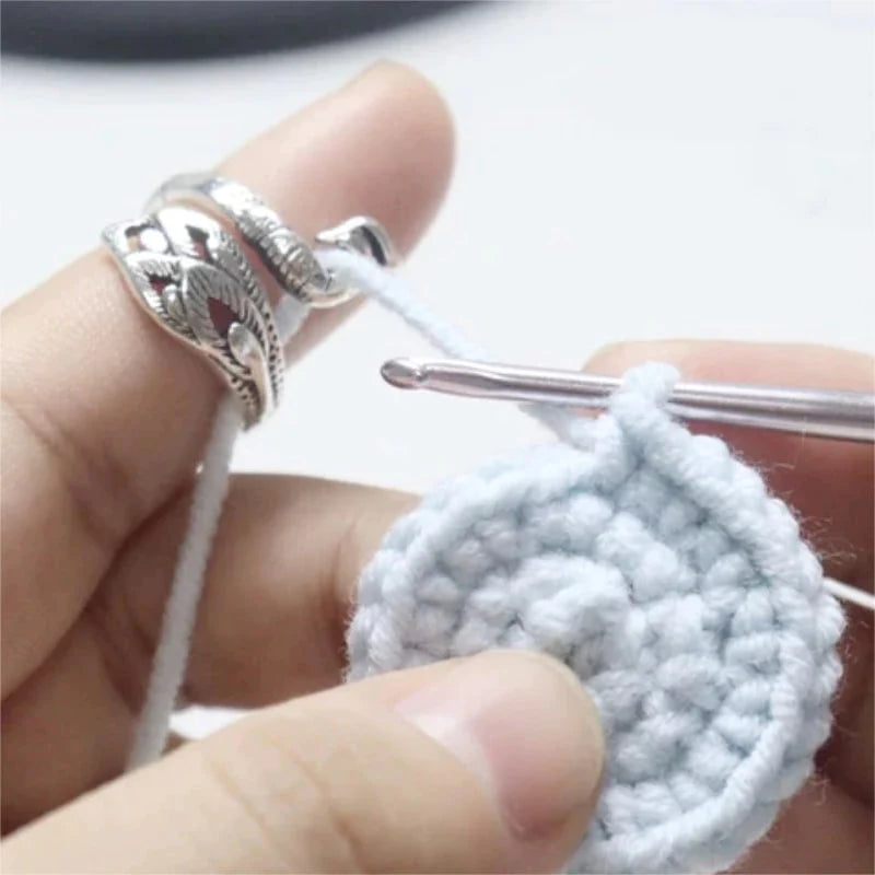 A person crocheting a small circular piece with precision, using a Yarn Tension Control Ring, a silver hook, and white yarn.