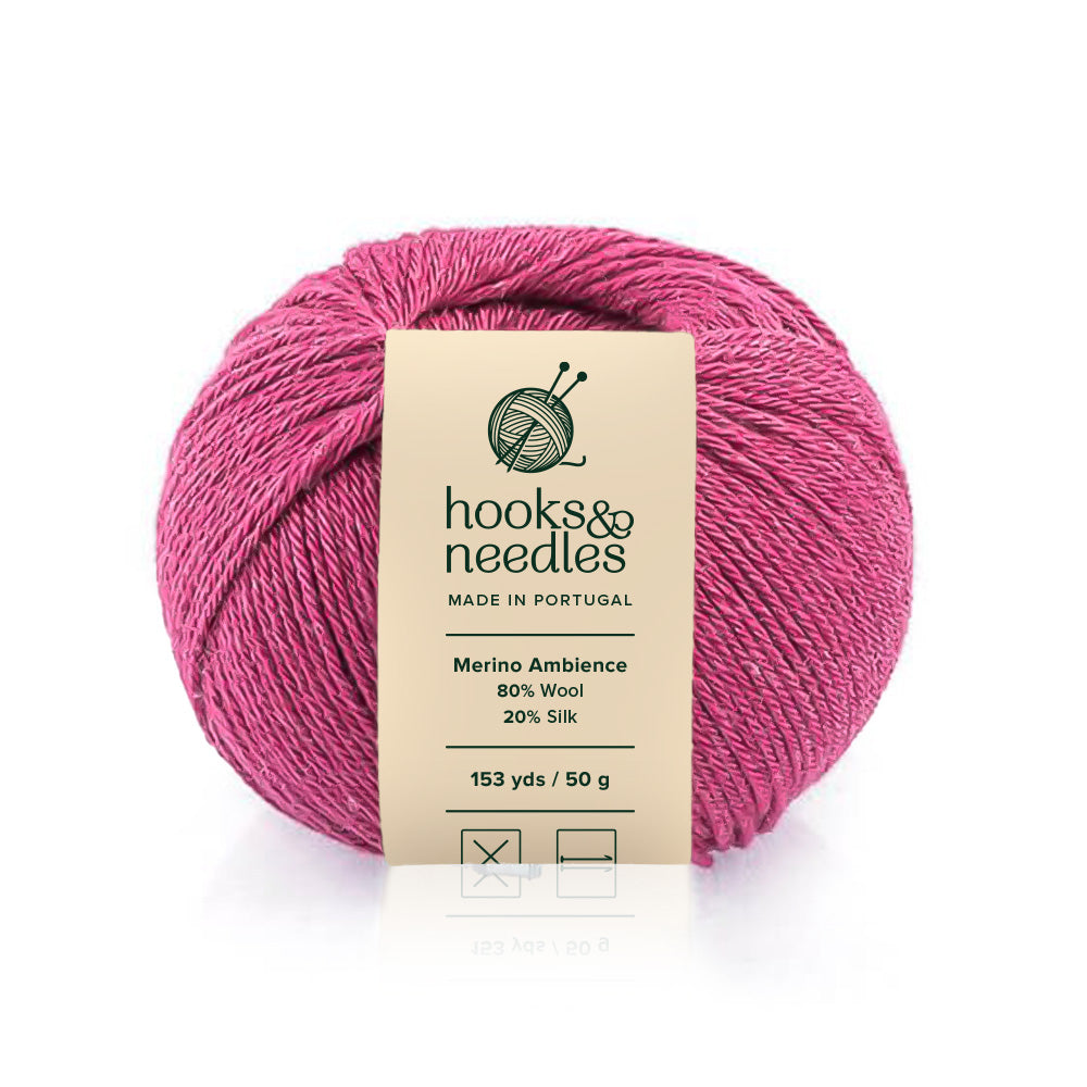 A skein of pink Merino Ambience yarn with a label indicating it's made in Portugal, consisting of 80% wool and 20% silk.