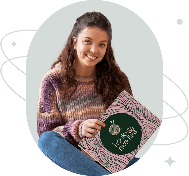 A smiling woman sitting cross-legged, holding a book with the title "hooks&needles"