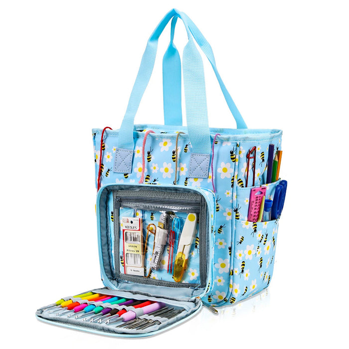 A light blue floral and bee patterned Multifunctional Knitting Tote Bag: Yarn Storage Organizer with multiple pockets. The front pocket is open, revealing various stationery items including pens, markers, glue, and scissors. Perfect for organizing your knitting supplies or using as a yarn storage organizer.
