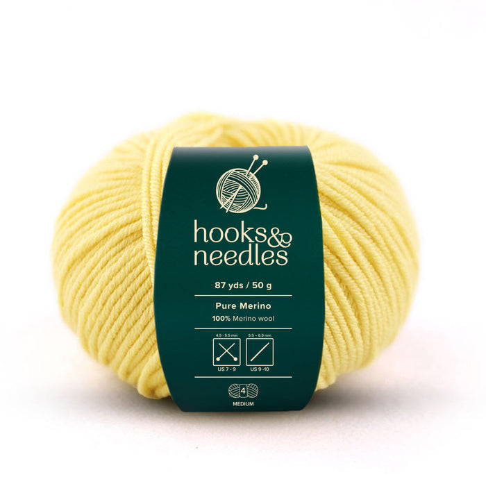 A 50g ball of medium-weight merino wool yarn in yellow, featuring a green label that displays the brand "Hooks & Needles" along with the weight, length, and recommended knitting needle sizes. Perfect for crafting cozy garments.