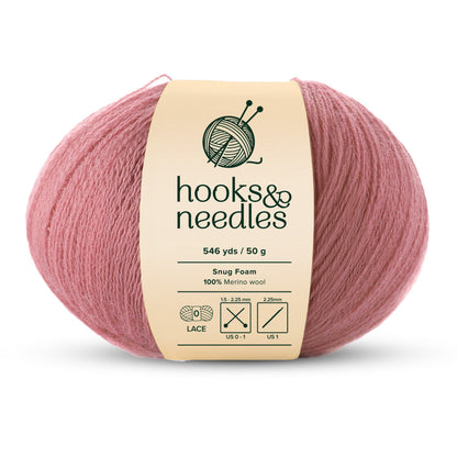 The Snug Foam Yarn 50g ball of pink merino wool lace-weight yarn provides 546 yards, perfectly suited for knitting and crochet projects with recommended needle sizes, and is labeled "hooks & needles.