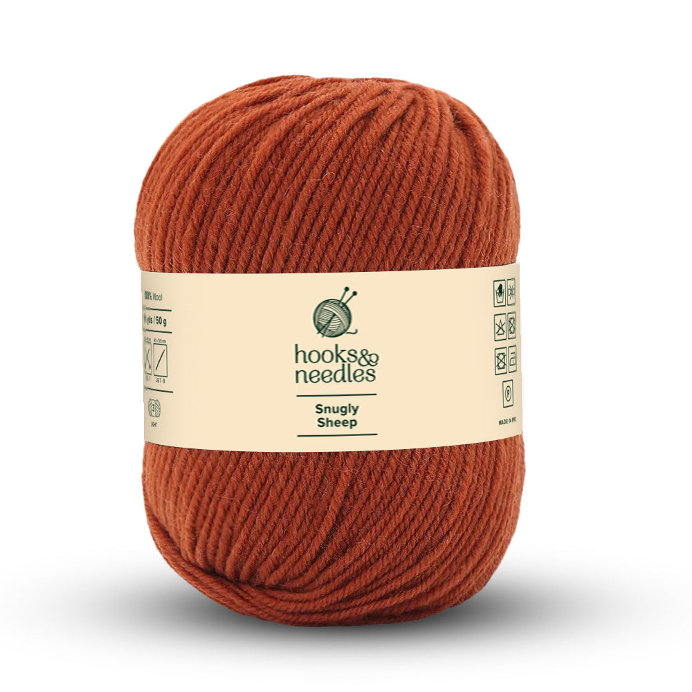 A ball of rust-colored Snugly Sheep Yarn 50g from the "hooks & needles" collection prominently features its 100% wool composition on the packaging. This lightweight yarn is perfect for your cozy crafting creations.