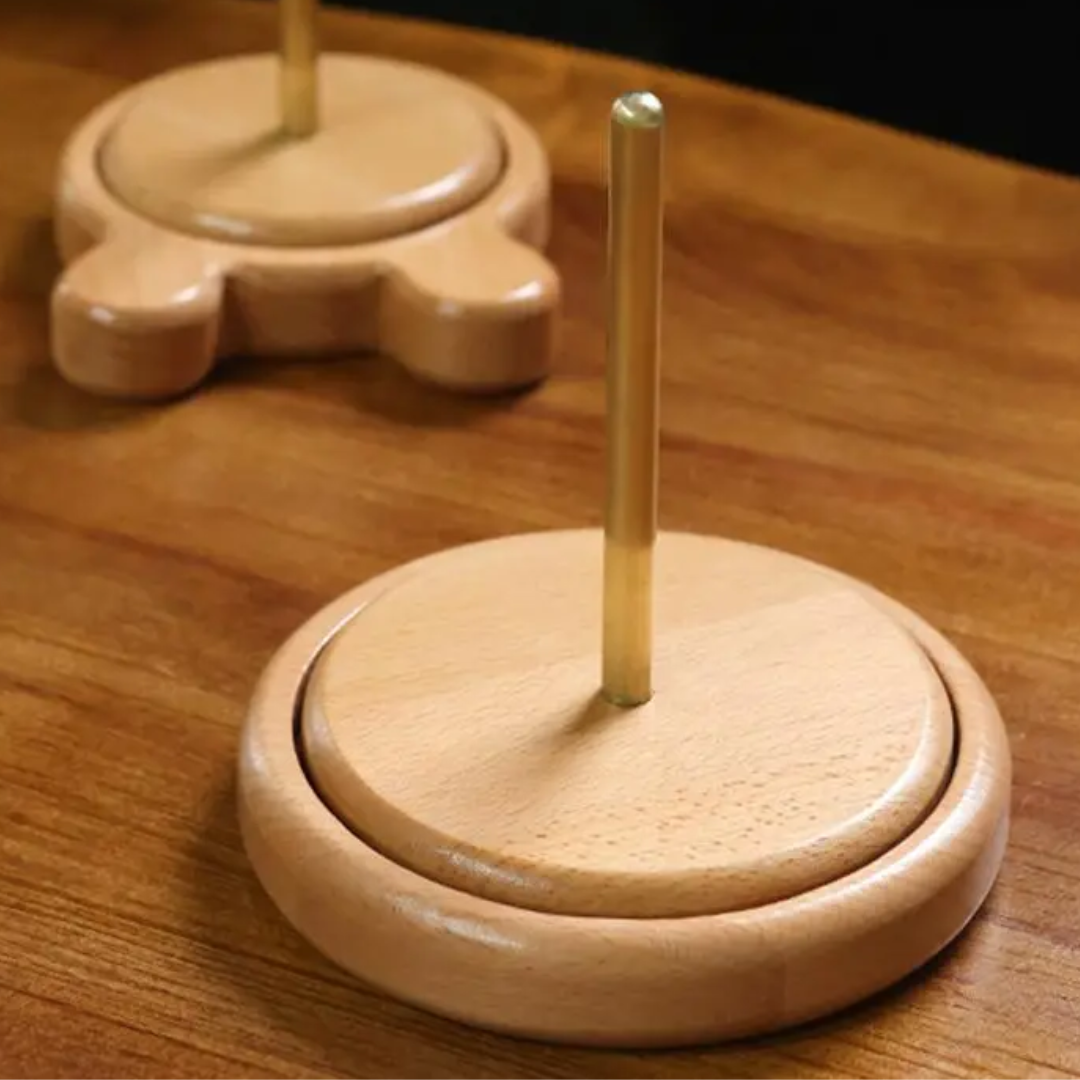 Two paper towel holders made of beech wood sit elegantly on the surface, one with a circular base and the other with a paw-shaped design. Their craftsmanship mirrors that of the Wooden Yarn Holder, combining style and practicality for efficient yarn management without tangles.