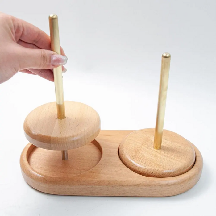 A hand places a wooden disk onto a vertical peg, which is part of the Wooden Yarn Holder made from beech wood, featuring two pegs to provide an elegant tangle-free yarn management system for your knitting projects.
