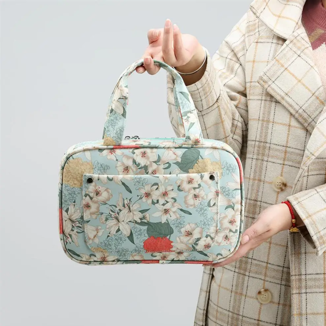 A person holding a Compact Tote Bag with a floral pattern and pocket, perfect for knitting supplies, while wearing a plaid coat.