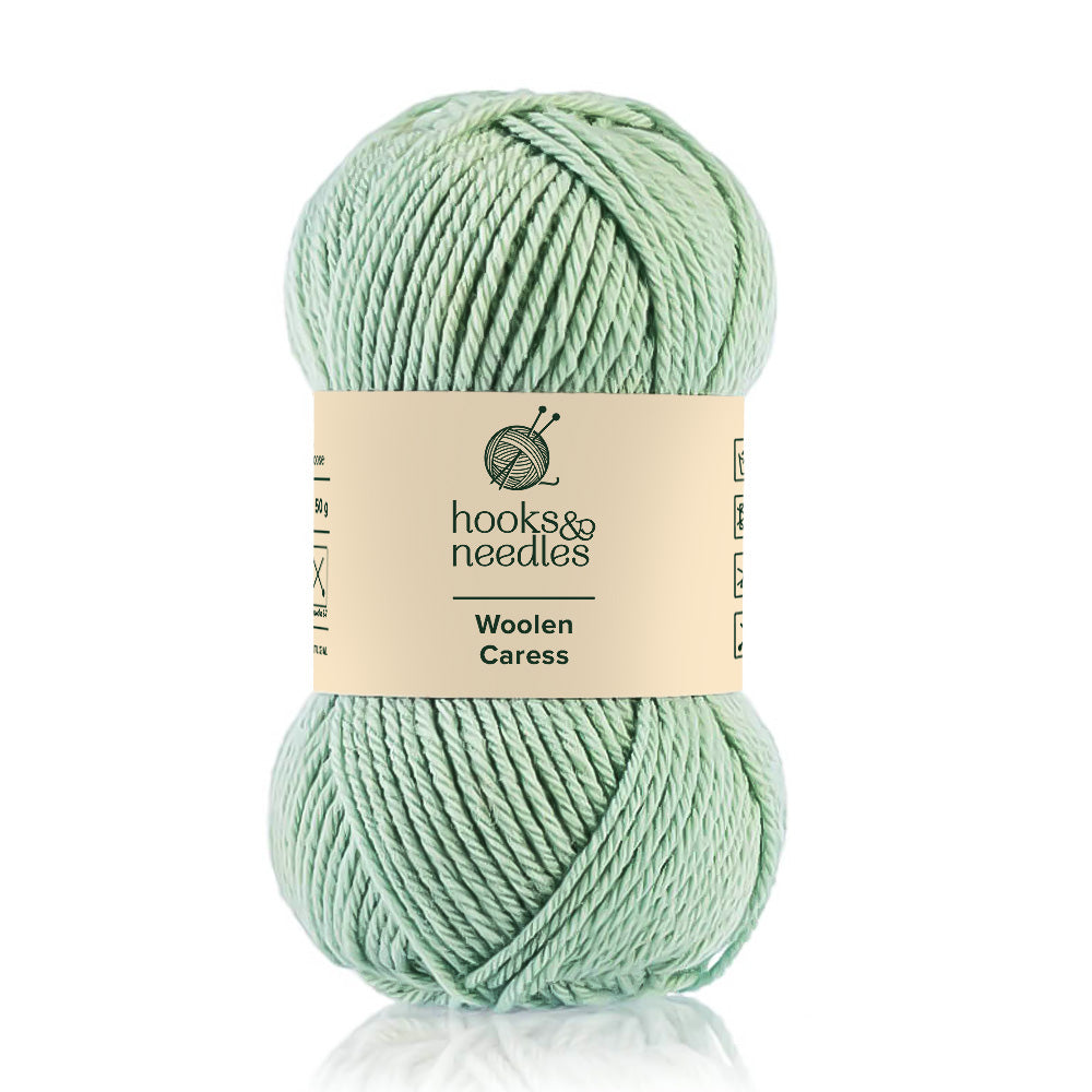 A skein of 100% wool, light green yarn labeled "Woolen Caress" by hooks & needles, known for its natural fiber durability.