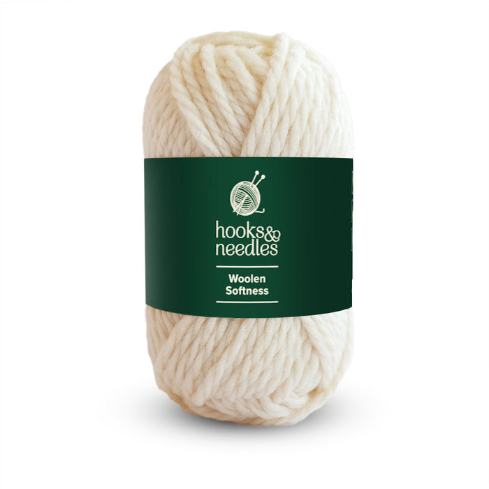 A skein of cream-colored, 100% wool yarn with a green label that reads "hooks & needles" and the product name "Woolen Softness Yarn 50g." Perfect for crafting chunky blankets, this super bulky yarn offers cozy warmth and softness in every stitch.
