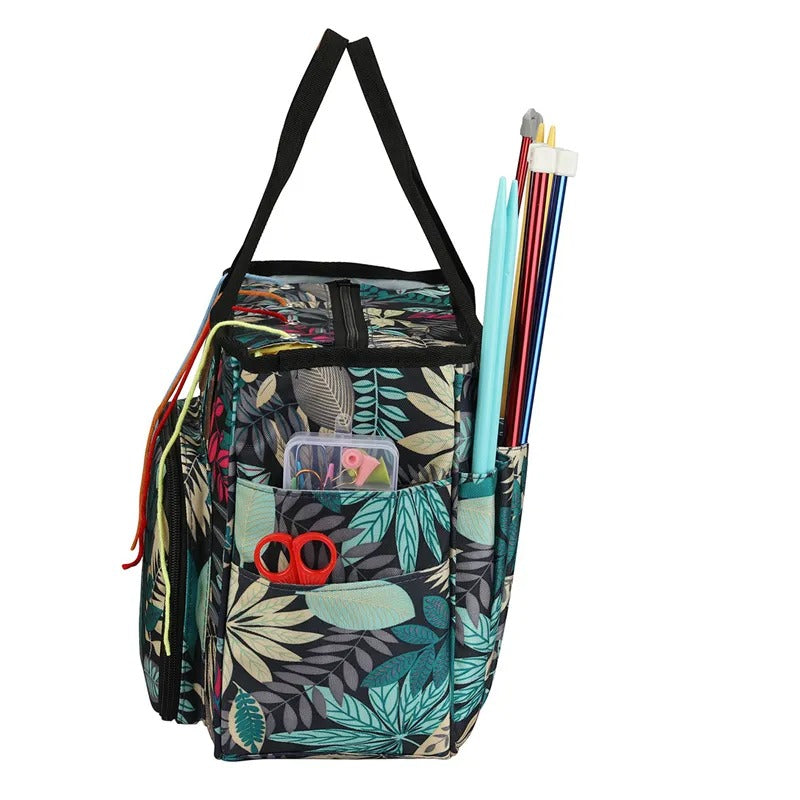 The Yarn Organizer Tote is a vibrant fabric bag featuring leaf patterns, designed to hold knitting needles, scissors, and other crafting tools in its side pockets.