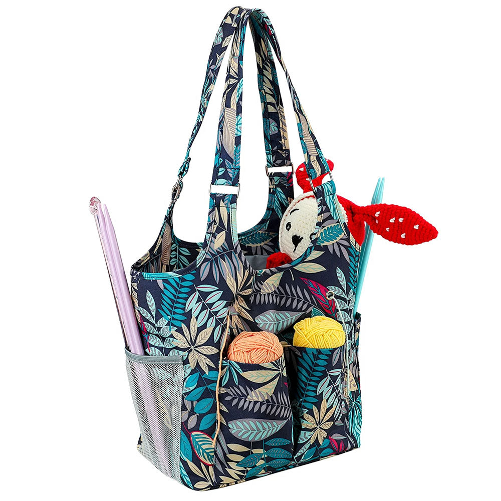 A floral-patterned Yarn Tote Bag: Knit on The Go filled with knitting essentials, including yarn balls, knitting needles, and a partially completed crochet animal. This knitting accessory also features visible side pockets.