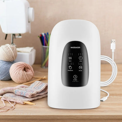 The Rechargeable Hand Massager with 5 Modes, featuring an ergonomic design and digital display, comes with a USB cable and sits on a wooden table next to knitting supplies—ideal for relieving hand fatigue during crafting sessions.