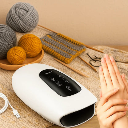 A person rubs their hands near the Rechargeable Hand Massager with 5 Modes, set on a table with yarn, knitting needles, and a knitted swatch—ideal for knitters seeking hand fatigue relief, with its USB cable beside it.