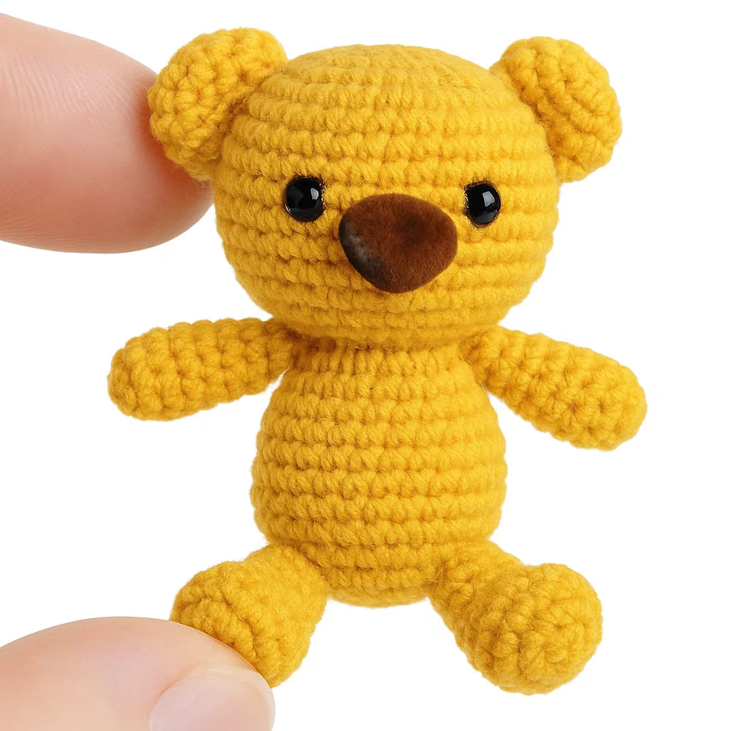 A hand displays a small, yellow amigurumi teddy bear featuring black eyes and a brown safety nose with washer, showcasing the "Safety Noses for Toys with Washers" product against a white background.