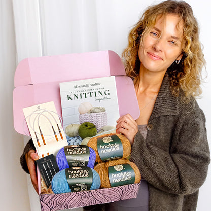Woman holding an open Hooks & Needles Subscription Box filled with knitting supplies and a magazine.