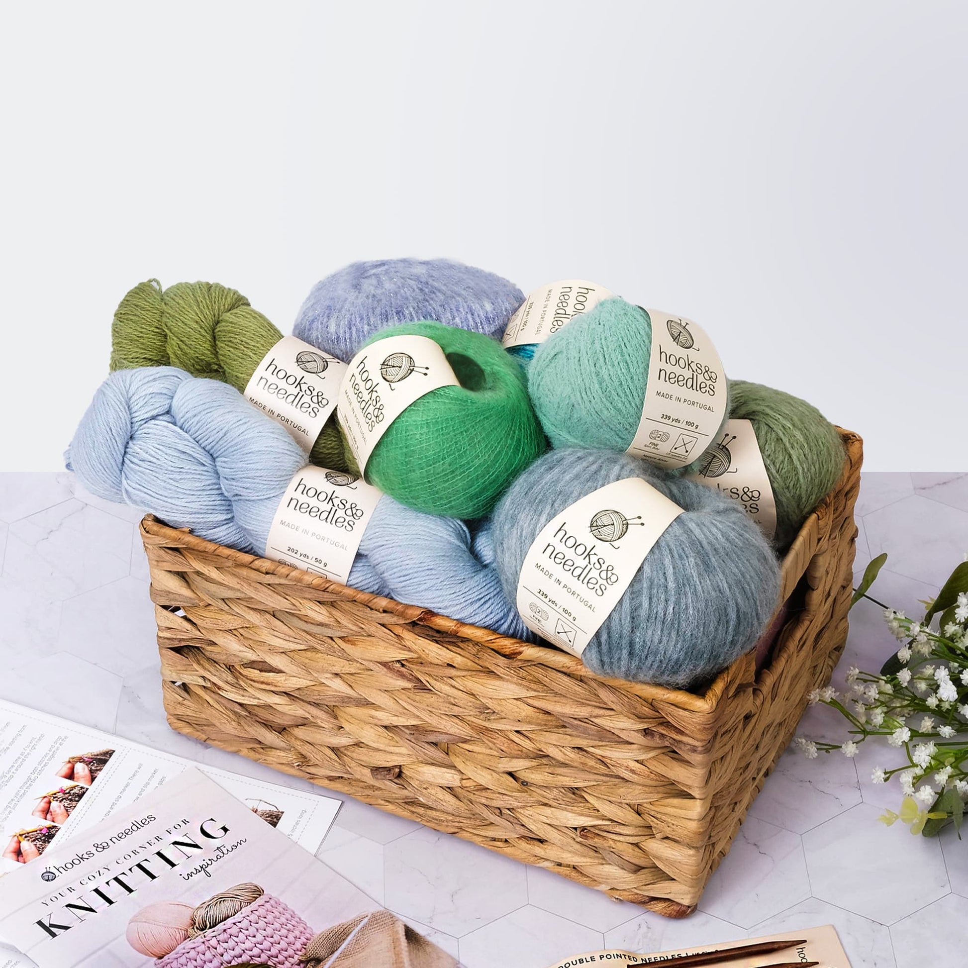 A Hooks & Needles Subscription Box in a woven basket with knitting magazines on the side.