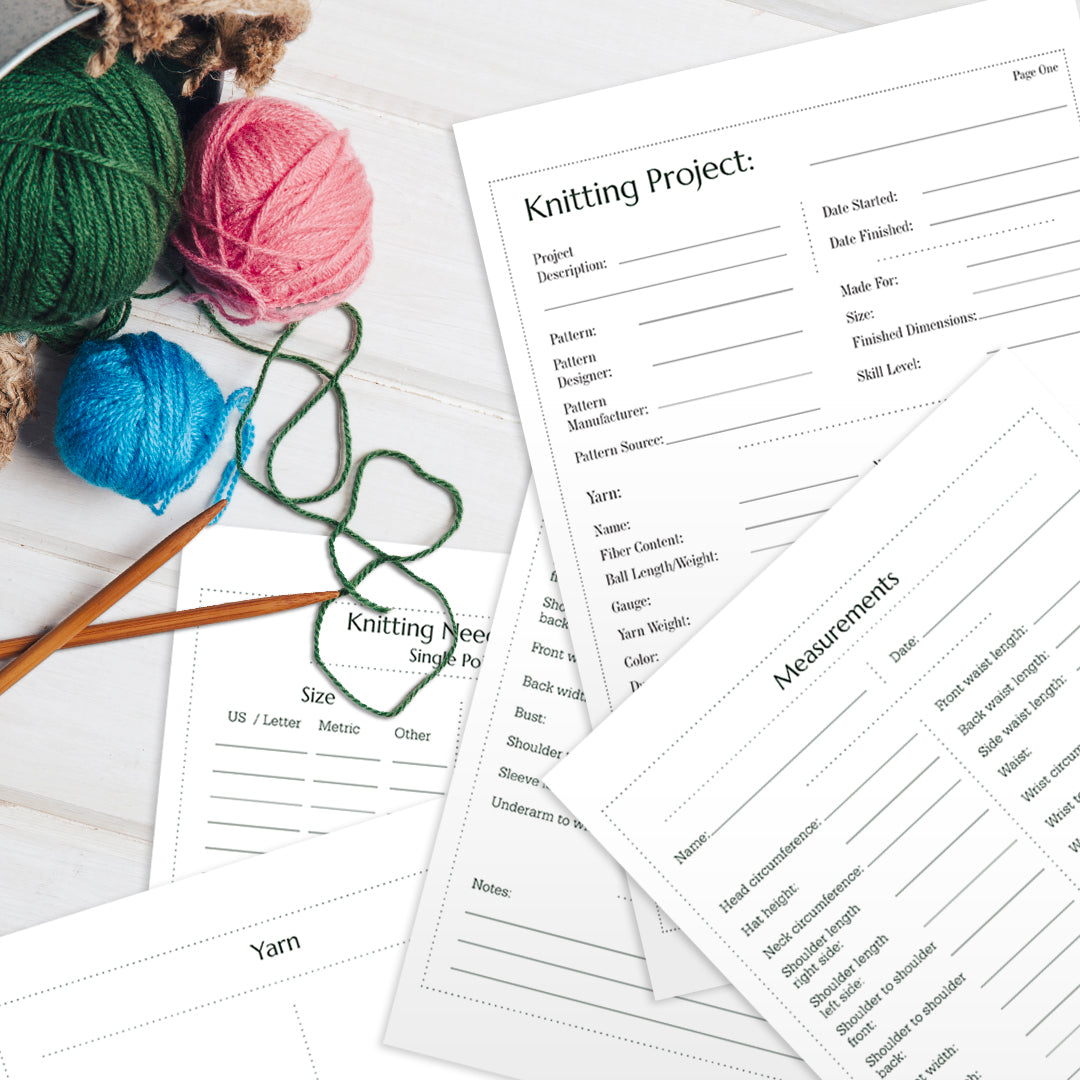 A collection of knitting project sheets, the Knitting Journal, yarn balls in green, pink, and blue, and wooden knitting needles on a white wooden surface.