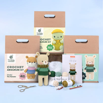 A display of the Amigurumi Subscription Box featuring different animal designs, accompanied by crochet supplies including yarn, a booklet, and scissors.