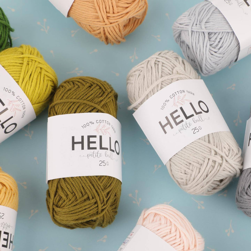 A selection of colorful yarn balls with "Hello" labels, arranged on a light blue surface from the Amigurumi Subscription Box.