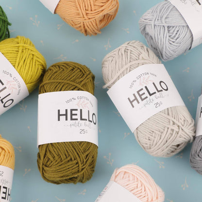 A selection of colorful yarn balls with "Hello" labels, arranged on a light blue surface from the Amigurumi Subscription Box.